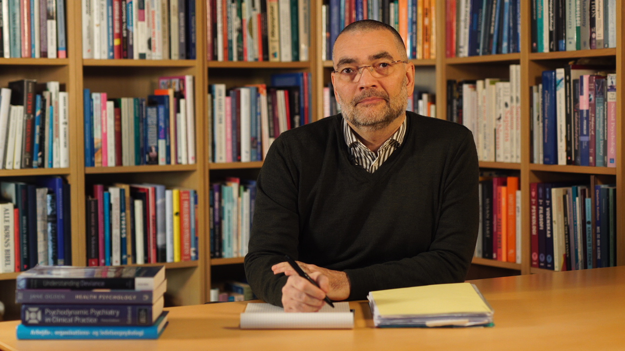 Ole Kondrup ved et bord foran en stor reol fyldt med bøger.